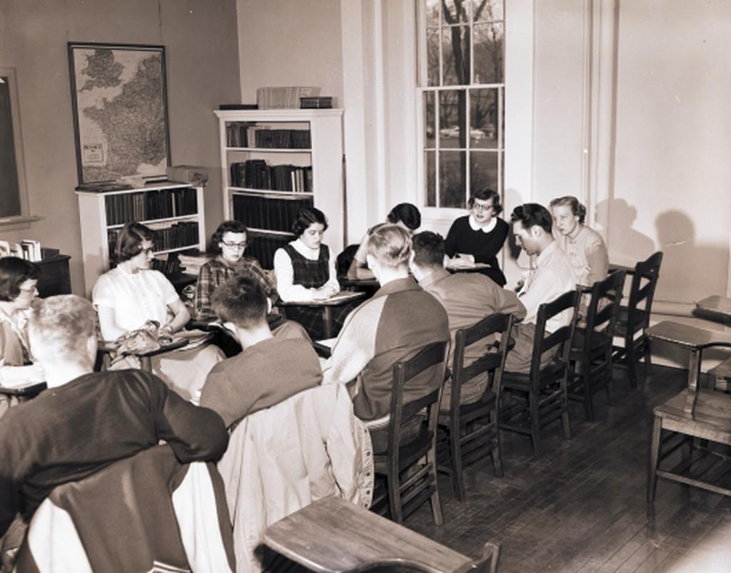 Black and white image of a classroom with students sitting around large conference table