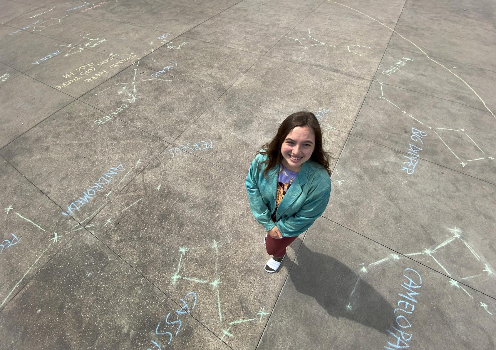 Avery Greene stands on a sidewalk decorated with chalk drawings of constellations.