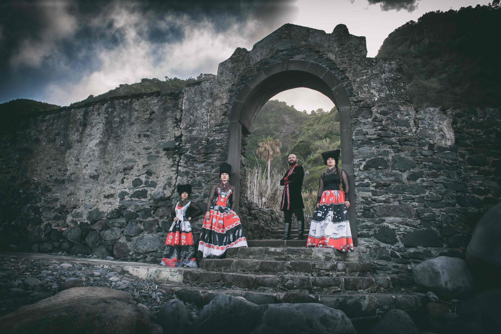 Musicians of DakhaBrakha standing underneath a stone arch, with blue sky above.