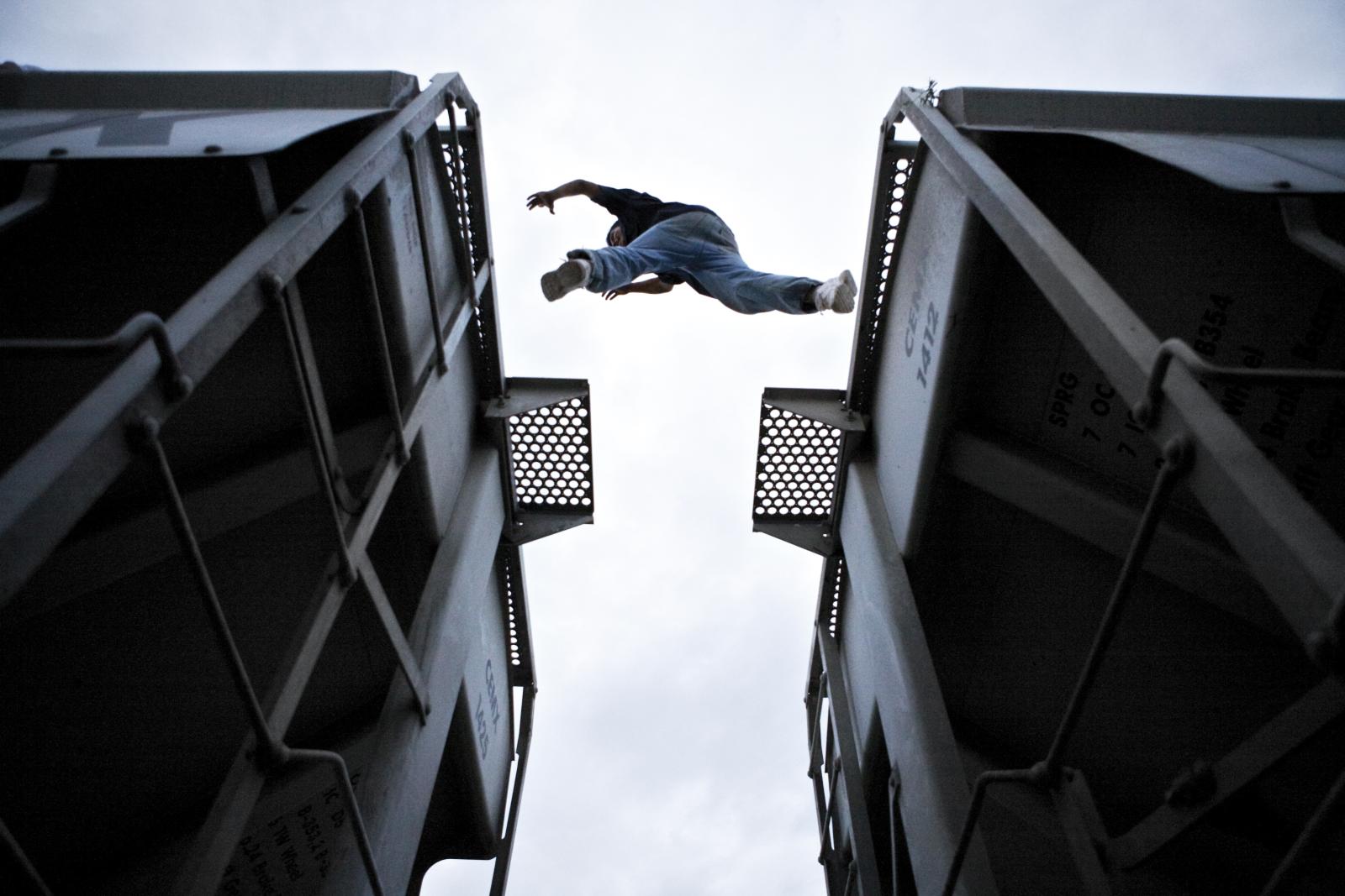 Man jumping between two train cars shot from below. 