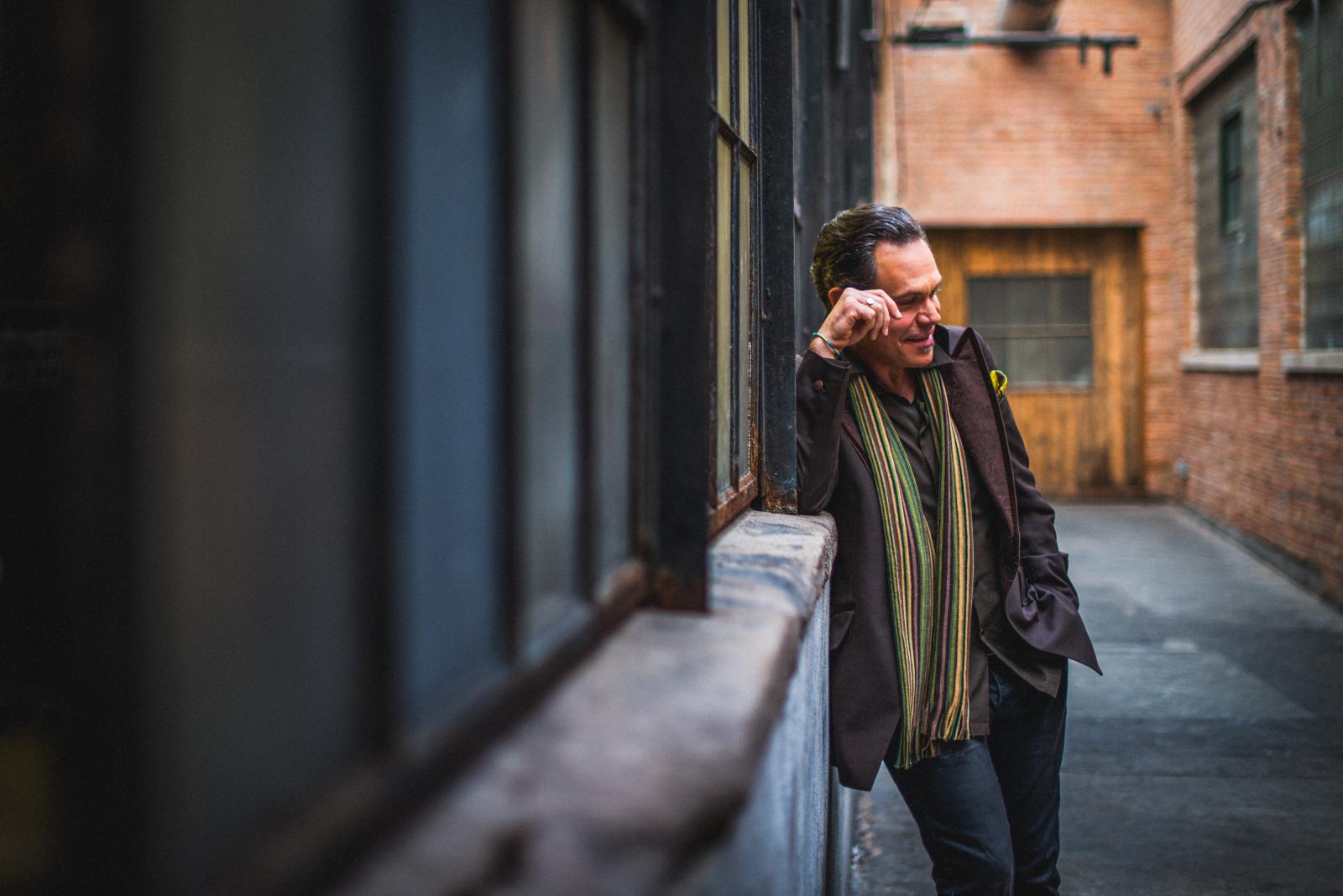 Musician Kurt Elling wearing a scarf and leaning against a building wall