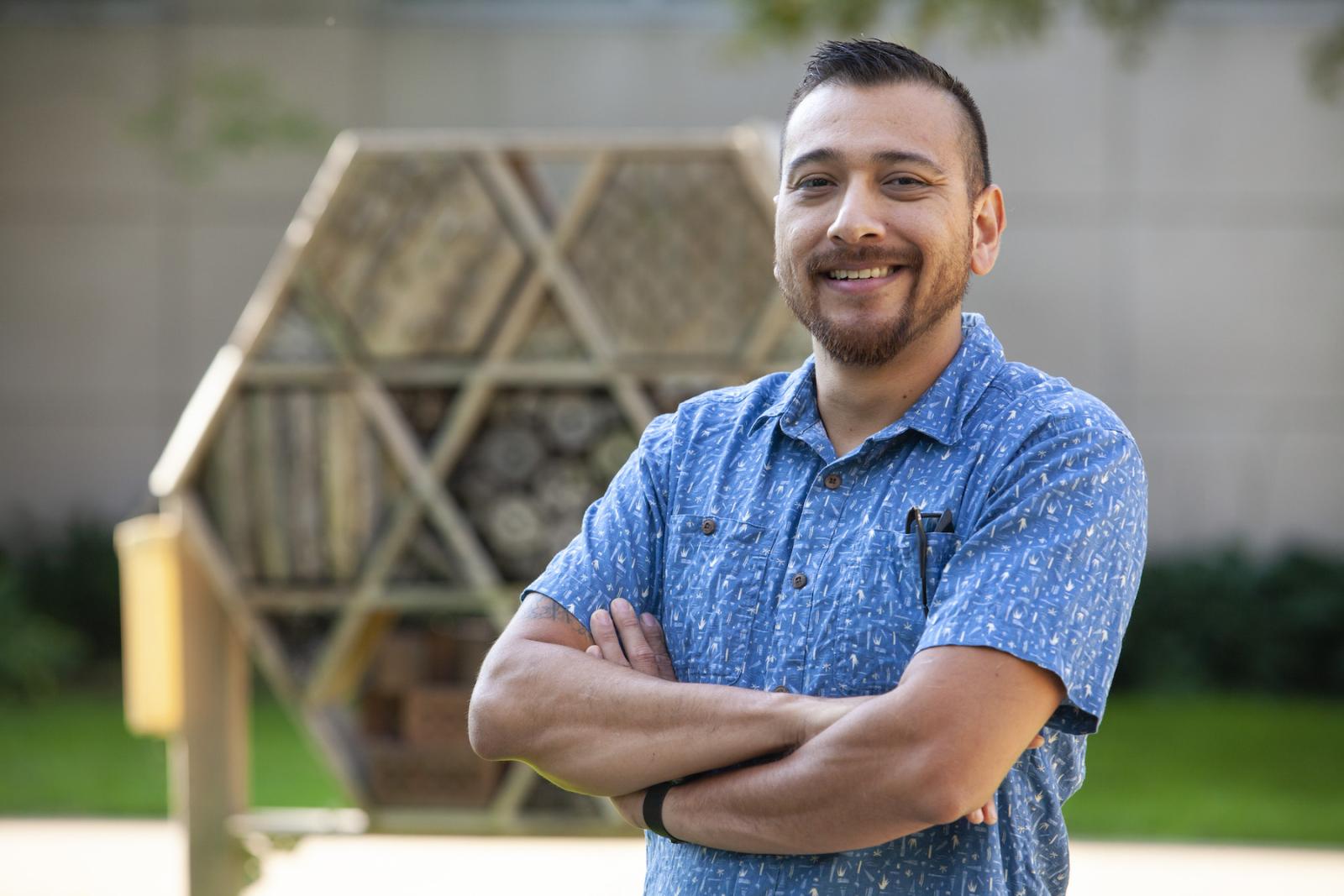 Israel Del Toro, wearing a blue shirt, stands in front of a bee-friendly structure.