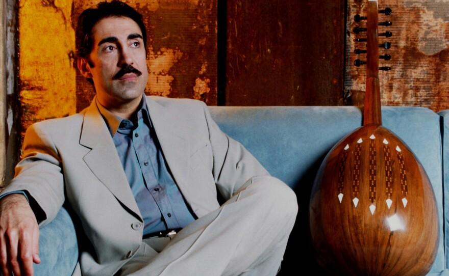 Musician Simon Shaheen sitting on a light blue couch with his instrument.