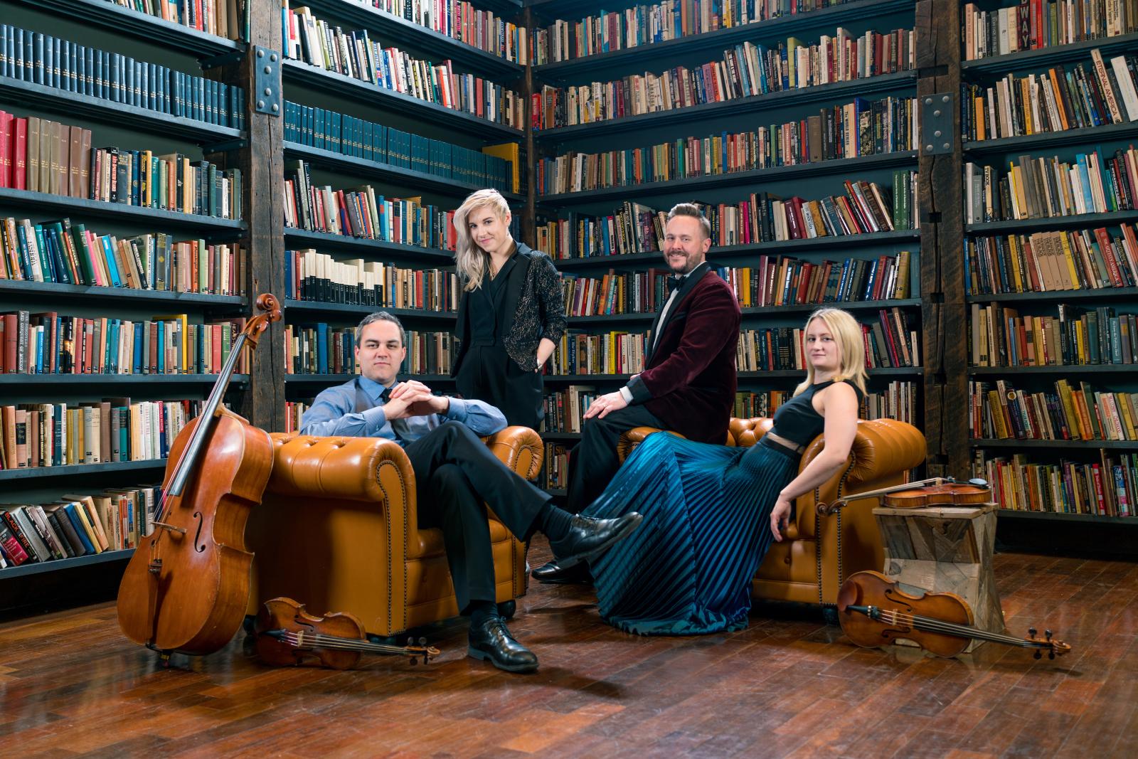 Musicians of Spektral Quartet seated in and on chairs in a room full of books. 
