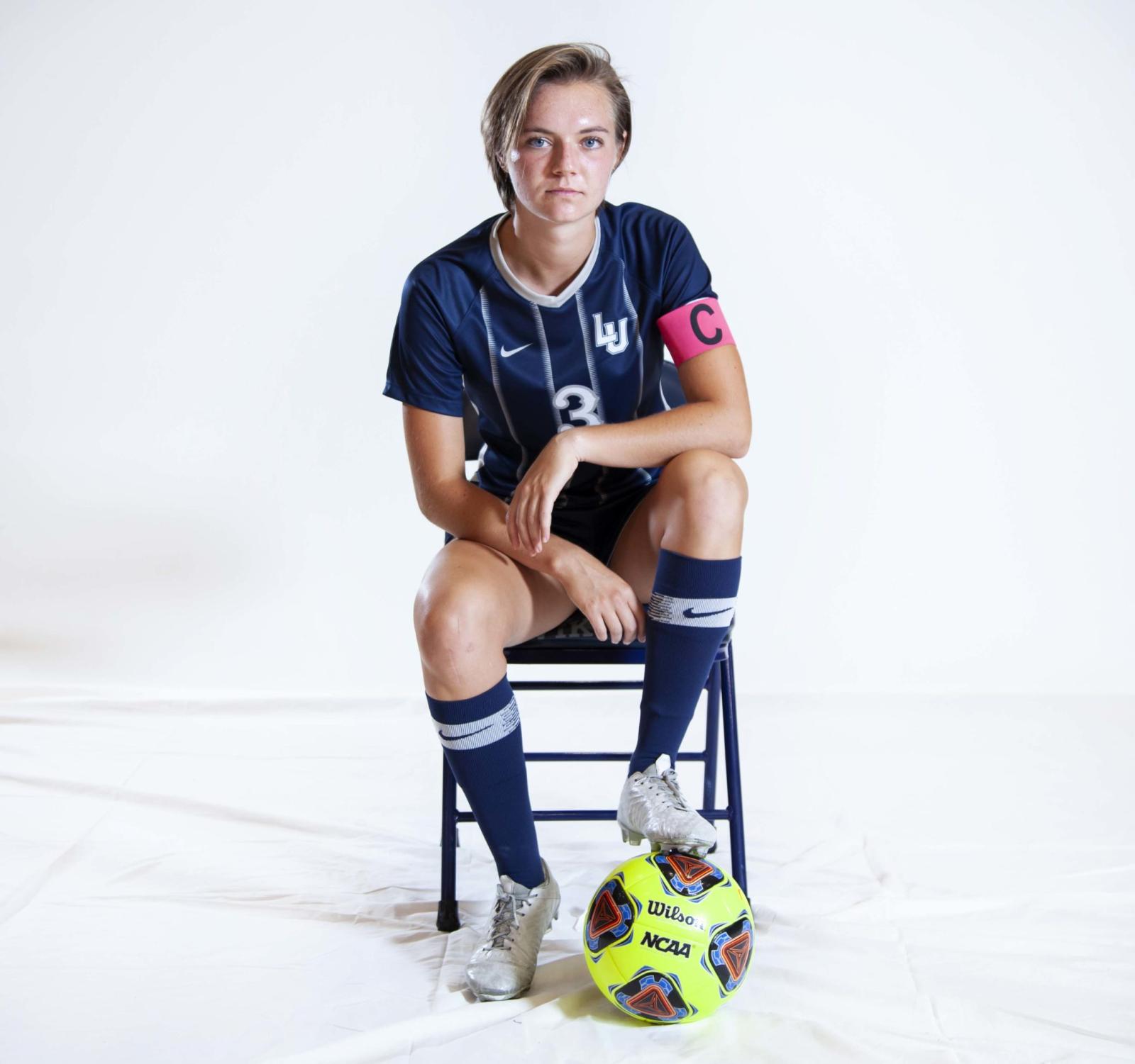 Soccer player Ellie Younger poses on a chair while holding a soccer ball under one foot.
