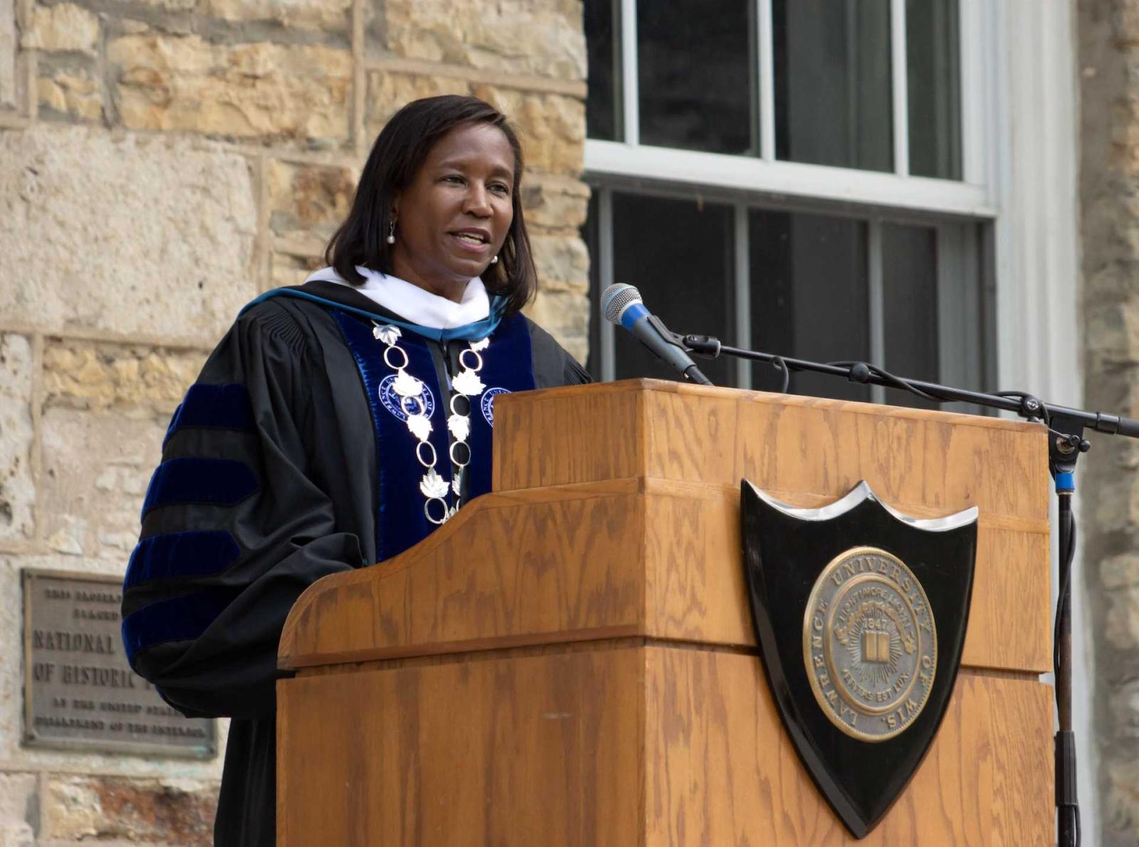 President Laurie A. Carter speaks into a microphone behind a lectern with Lawrence's seal on it.