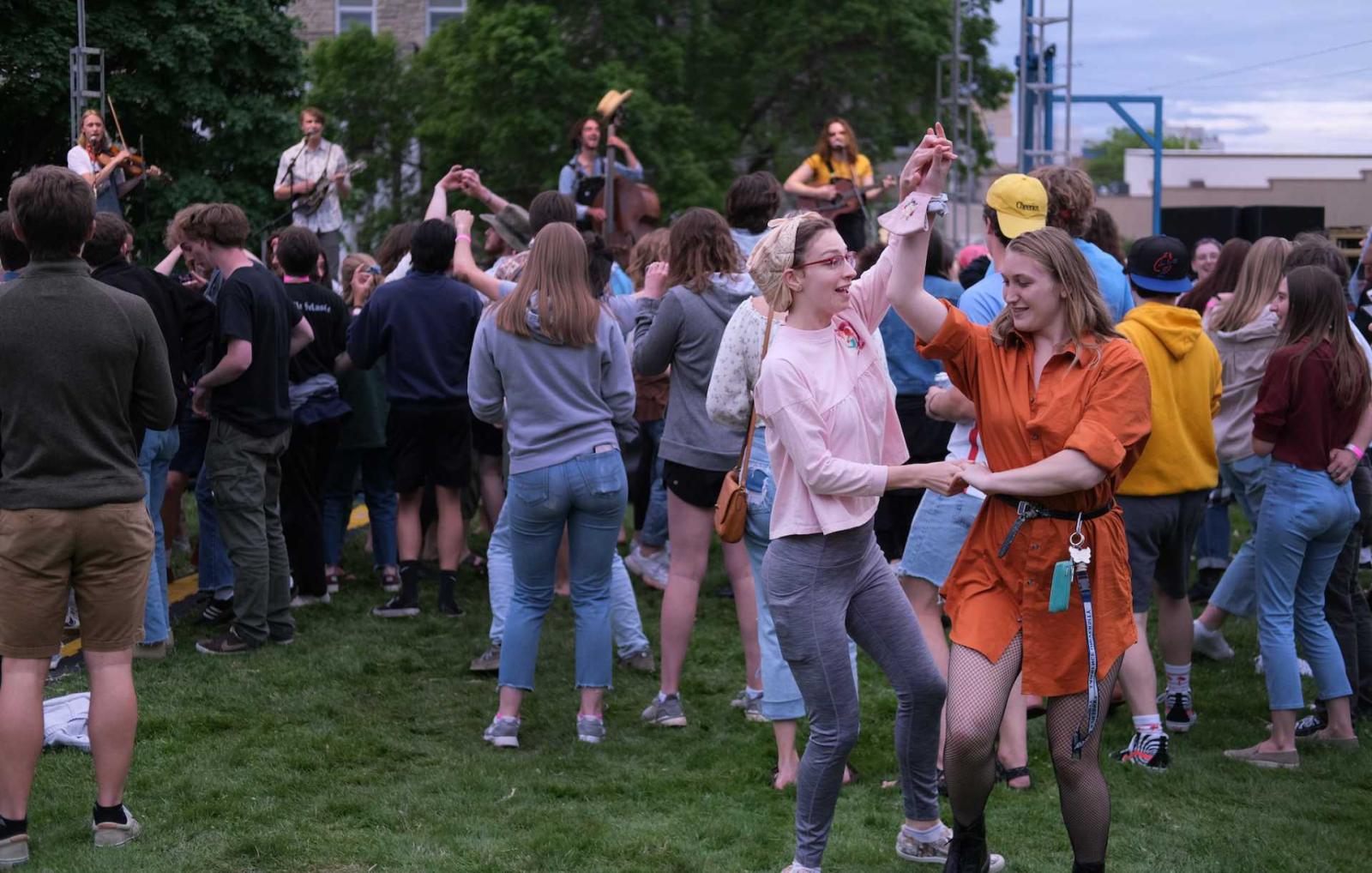 Students dance on lawn while bluegrass group performs in background onstage