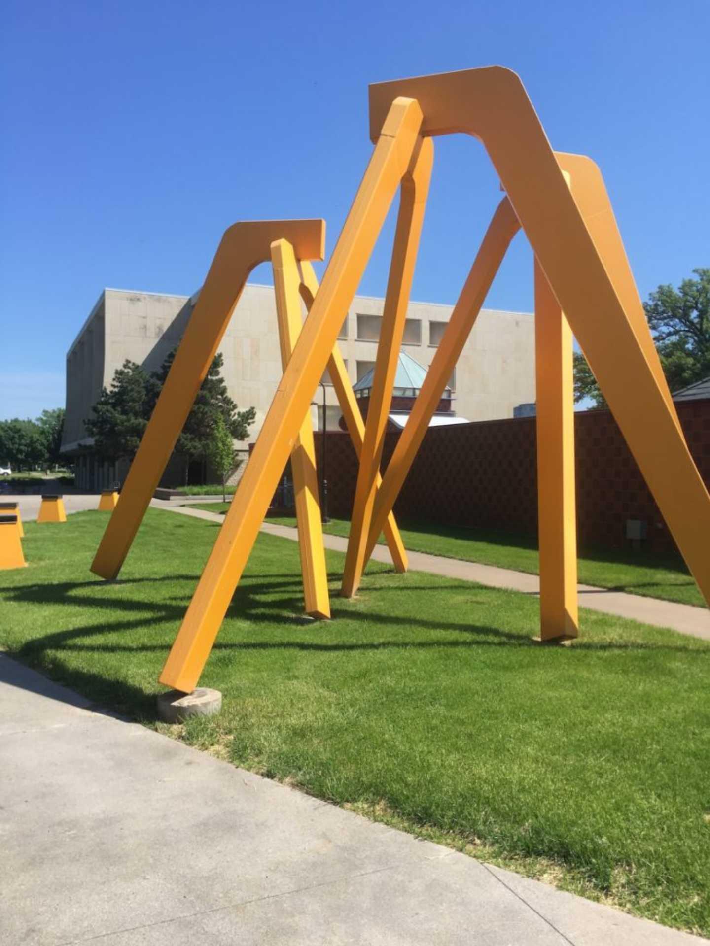 A trio of large, bright yellow tripartite arches, placed close to each other on a patch of green grass.