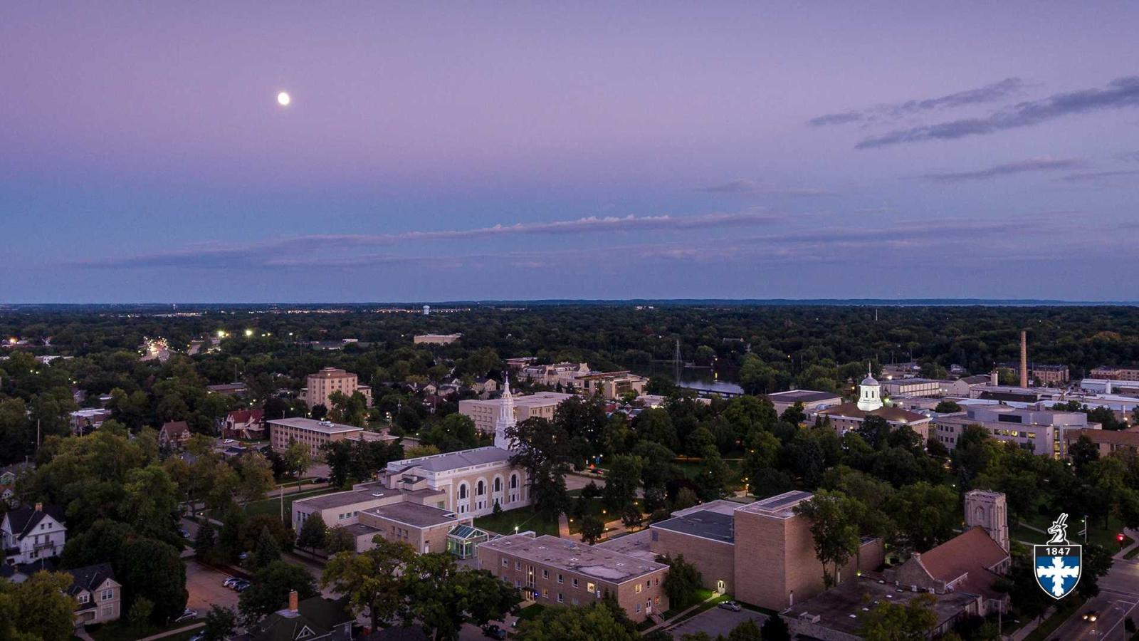 Aerial of campus at dusk with moon in the distant sky.