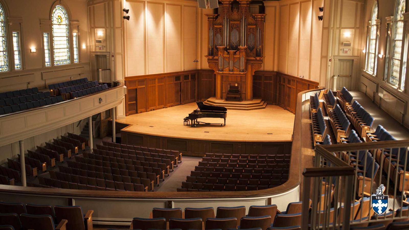 A grand piano stands center stage with organ in background inside an empty Memorial Chapel.