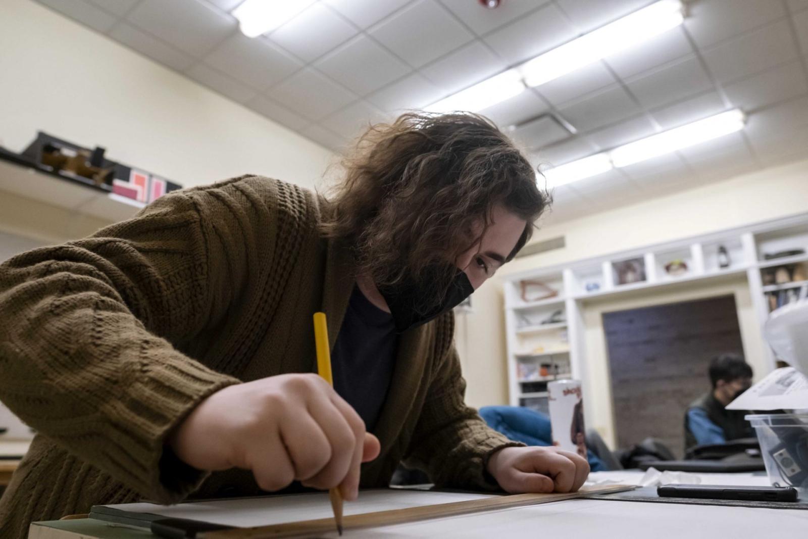 A seated student draws on a large piece of paper with a pencil.