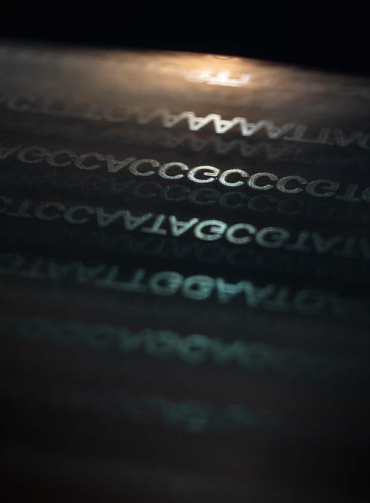 Letters describing a genetic code etched onto glass, dramatically lit against a black background.