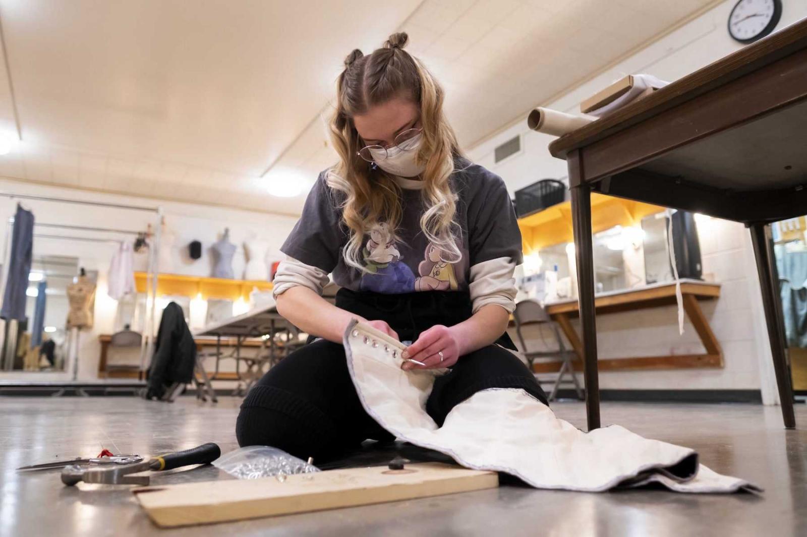 Sophia Driessen, a senior, sits on the floor as she works on a corset in the costume shop.