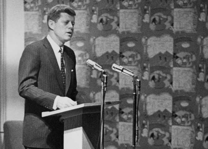 John F. Kennedy speaks at a podium in Riverview Lounge.