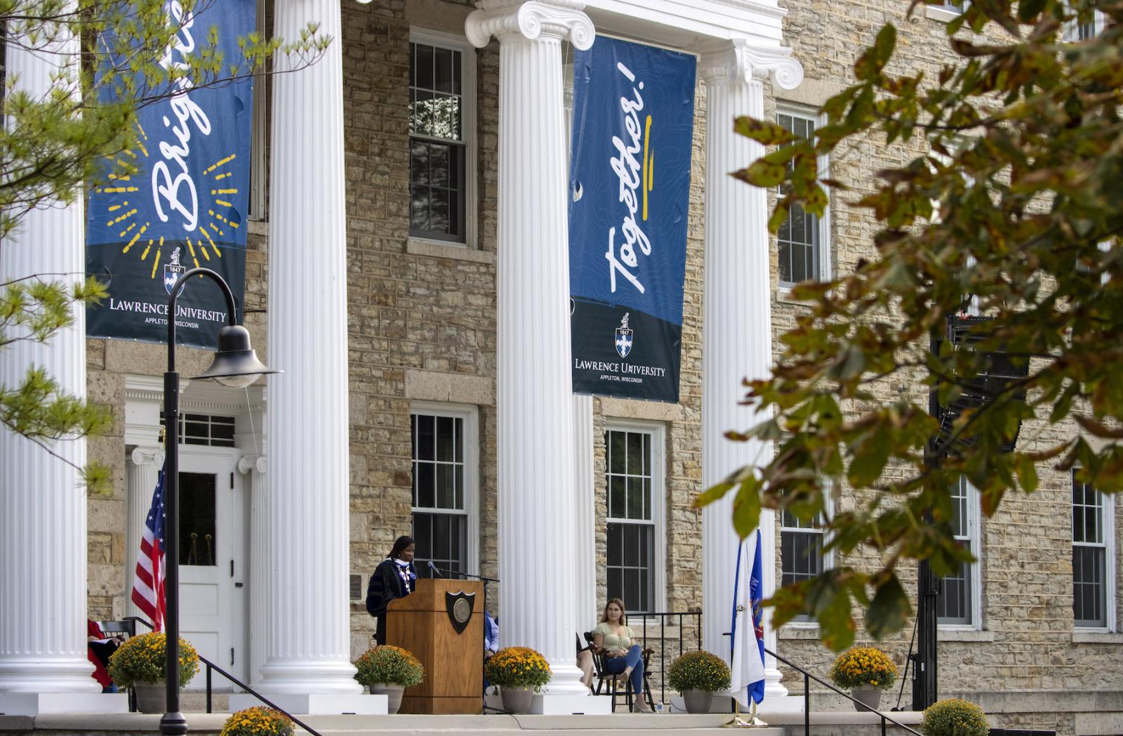 President Laurie A. Carter stands between Main Hall's columns sporting "brighter together" signs.