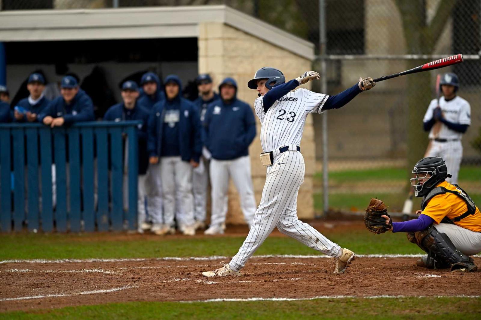 Lawrence baseball player Jacob Charon swings at a pitch as teammates look on.