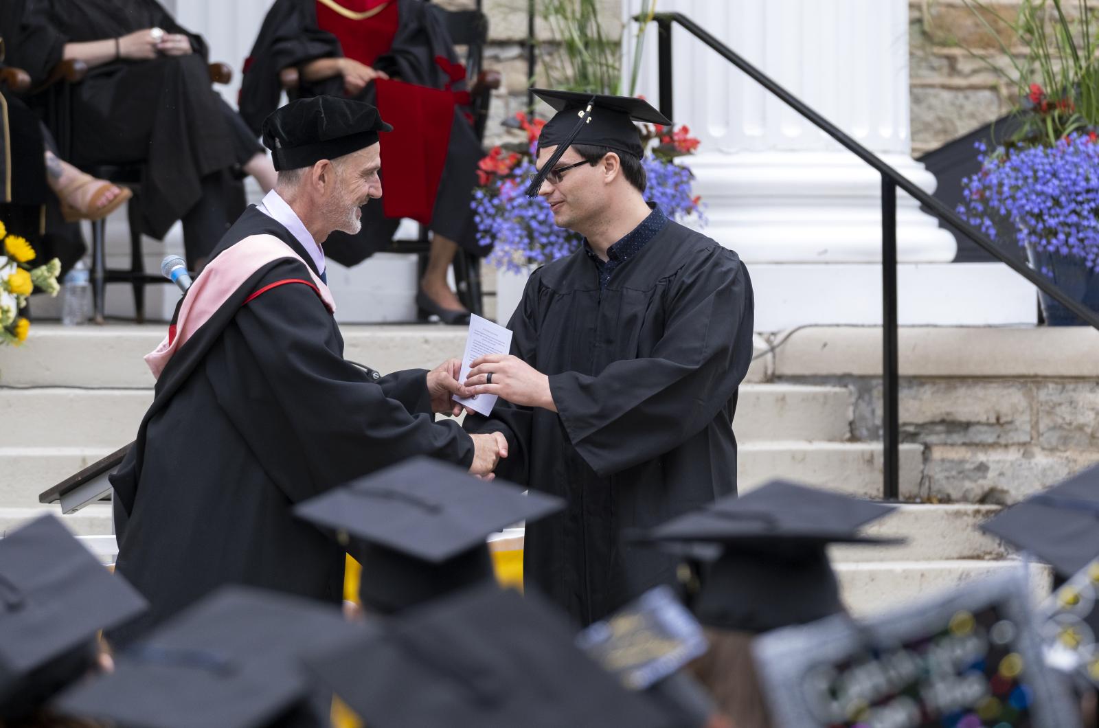 Brian Pertl shakes the hand of a 2020 graduate. Both are dressed in regalia.