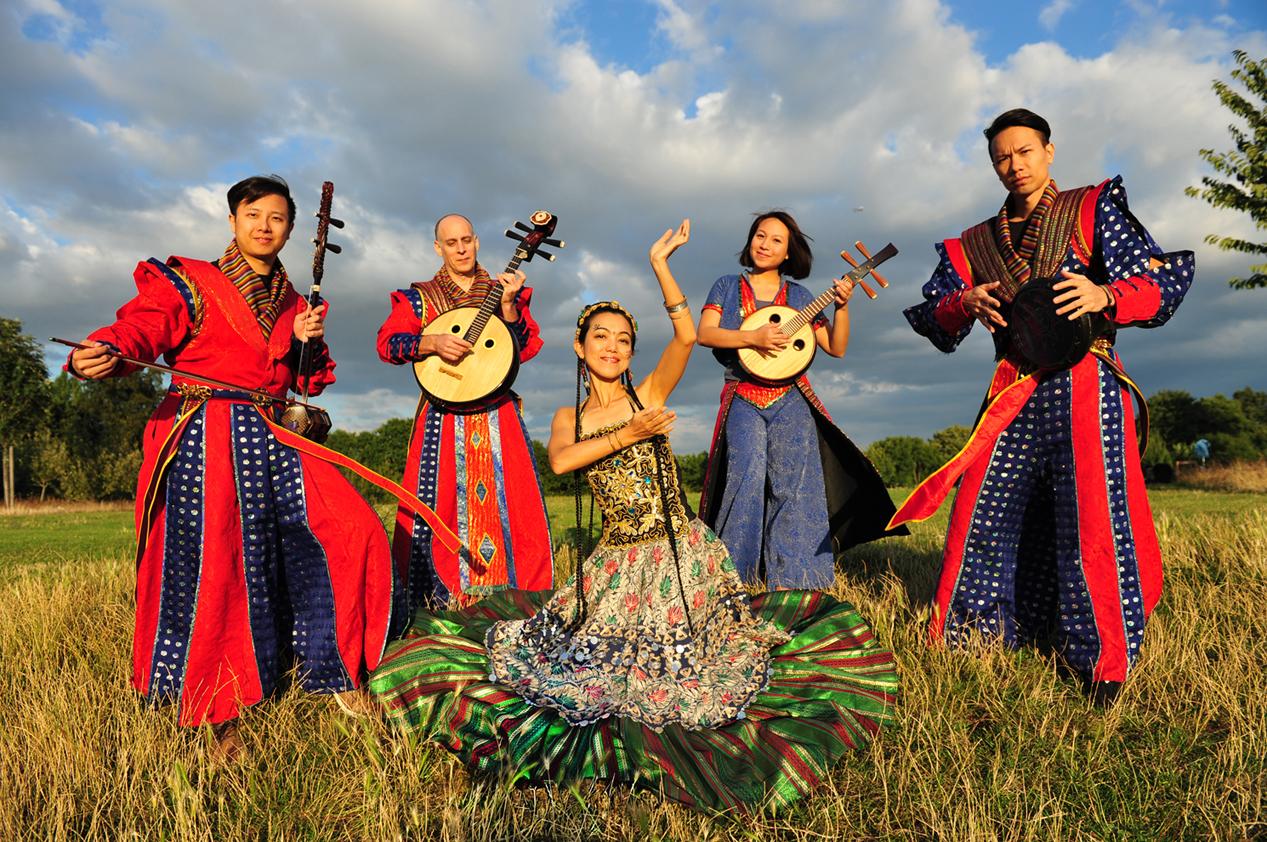 Four musicians of A Moving Sound stand in a field with their instruments, the dancer of the ground poses in the middle.