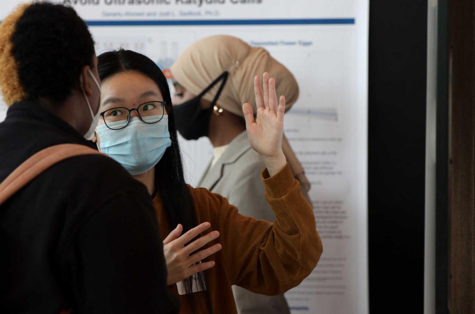 April Nguyen raises her hand as she explains her research to a student visiting her board. 