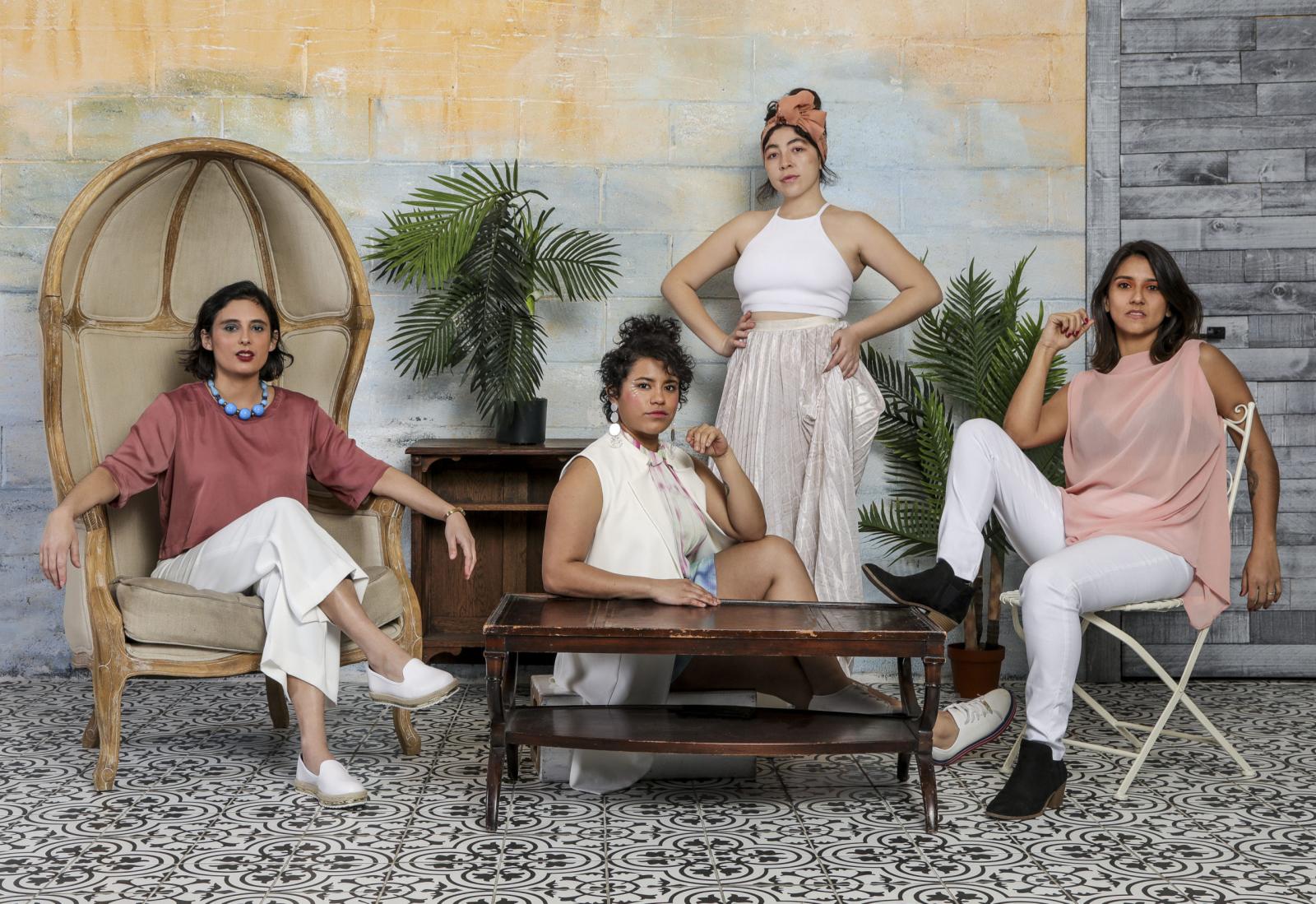 The four performers of LADAMA arrayed in a room, one in a high-backed wicker chair, one standing, one sitting on the floor and another in a wire chair. 