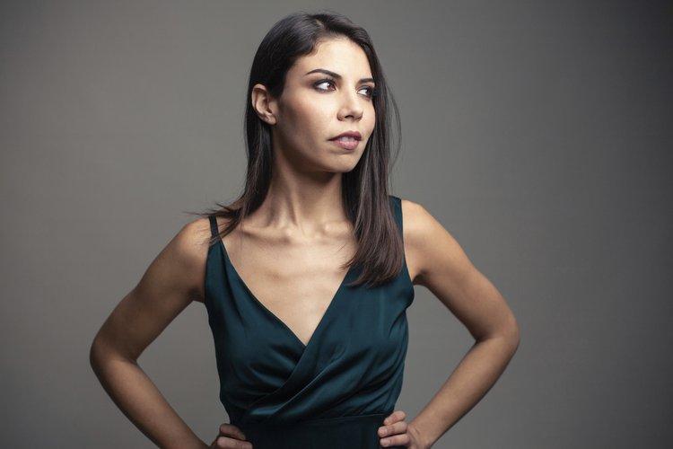 Saxophonist Melissa Aldana stands wearing a dark green dress in front of a grey background