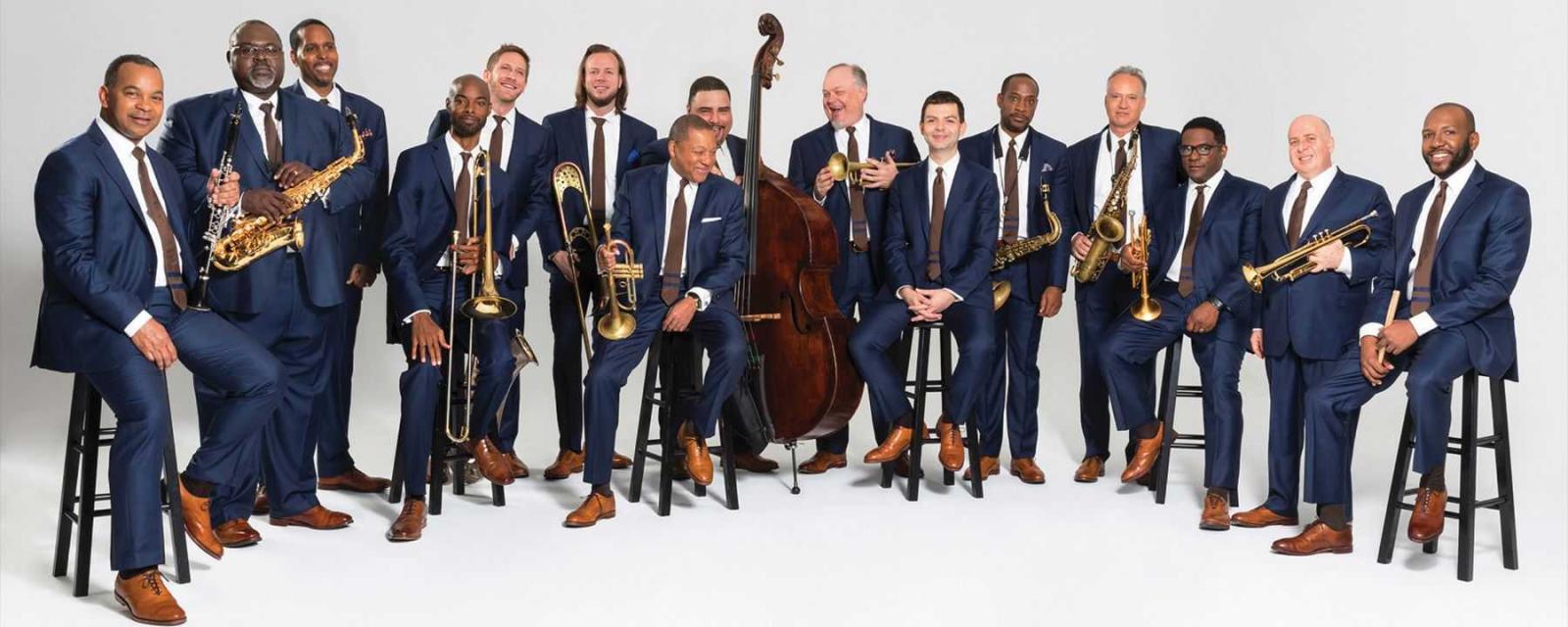 Wynton Marsalis sits on a stool surrounded by members of the Lincoln Center Jazz Orchestra.