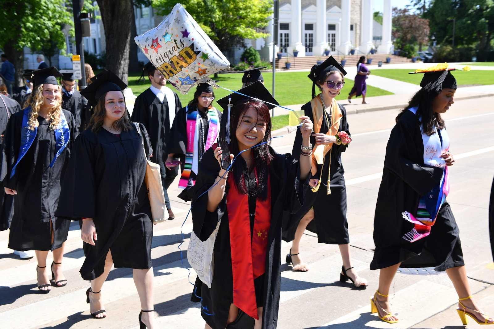 A graduate holds a Congrats Grad balloon as she and other graduates walk across College Avenue during the 2022 Commencement.
