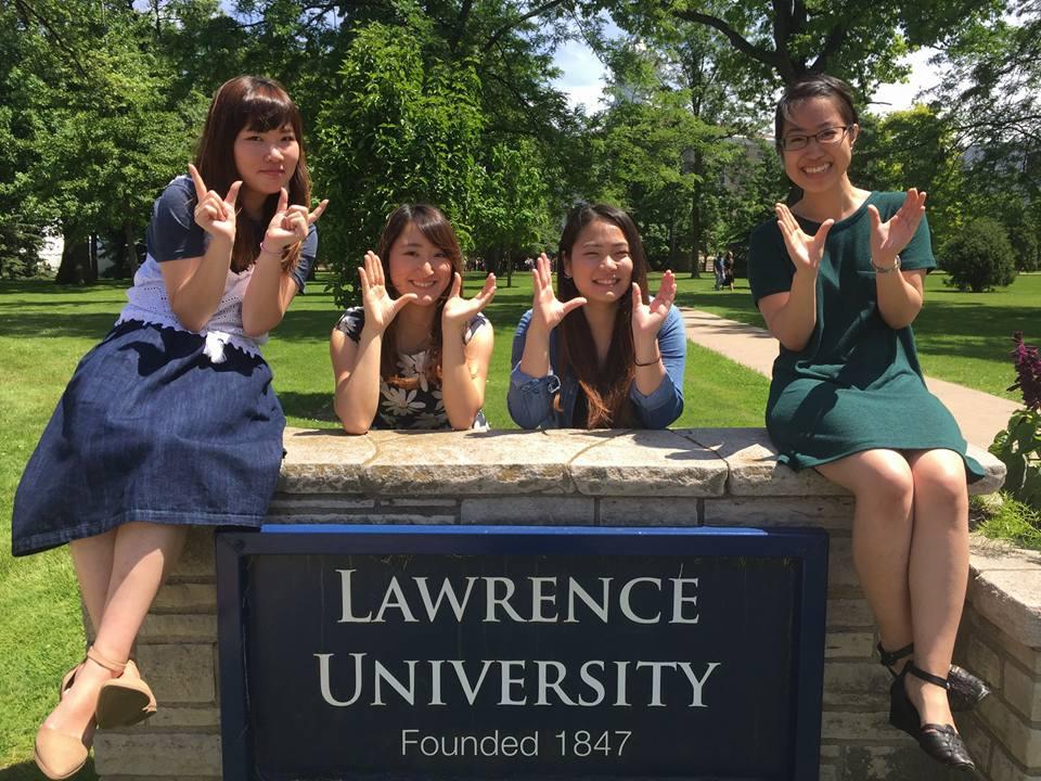 Four students sitting around Lawrence University sign making the letters LU with their hands.