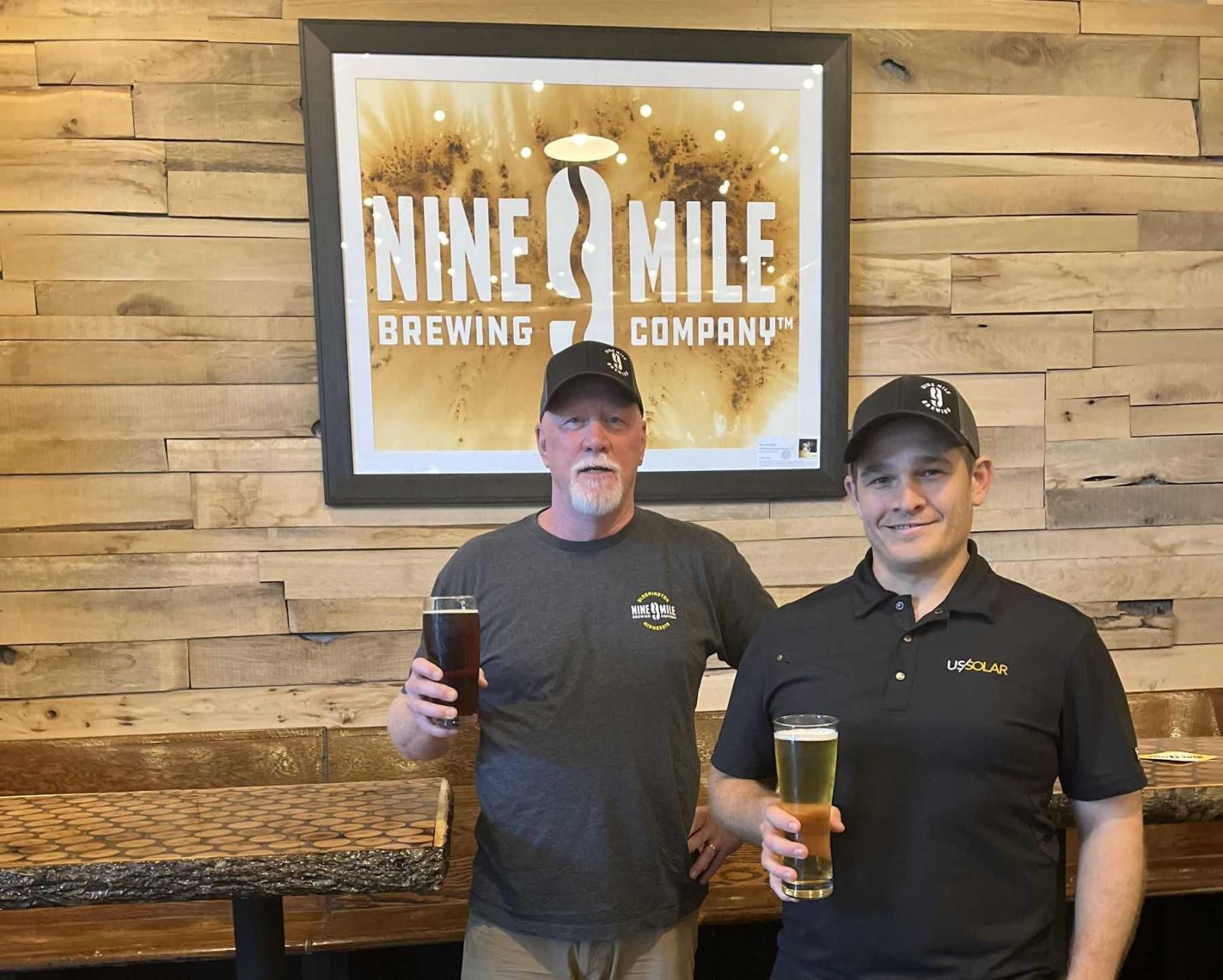 Bob Countryman and Ilan Klages-Mundt hold beers in front of a Nine Mile sign in their brewery.