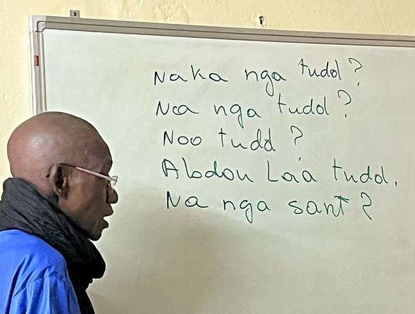 Senegalese teacher in front of white board teaching Wolof