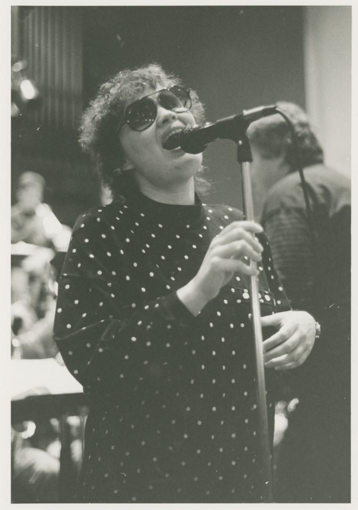 Women in sunglasses sings into microphone