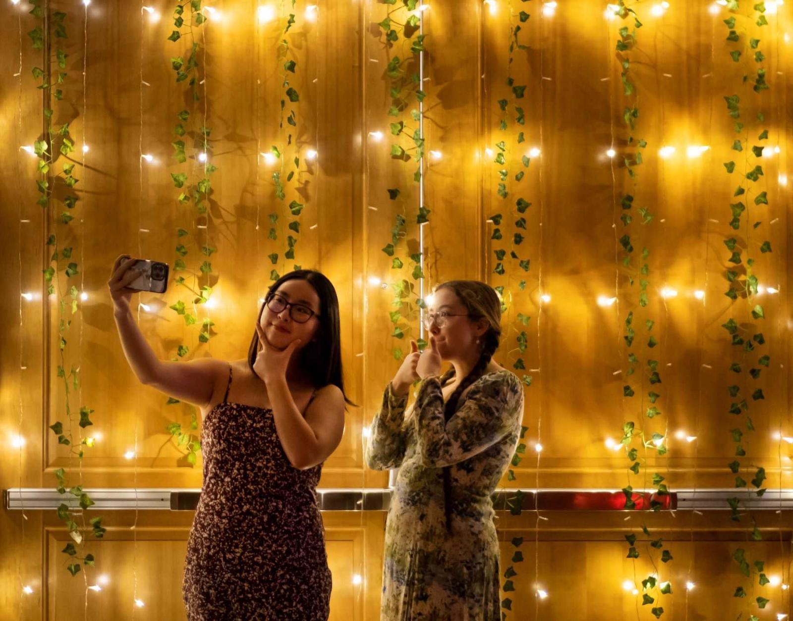 Rachel Joo and Fiona Kaiser, both juniors, pose for a photo in front of a wall of lights at the Fall Homecoming Dance.