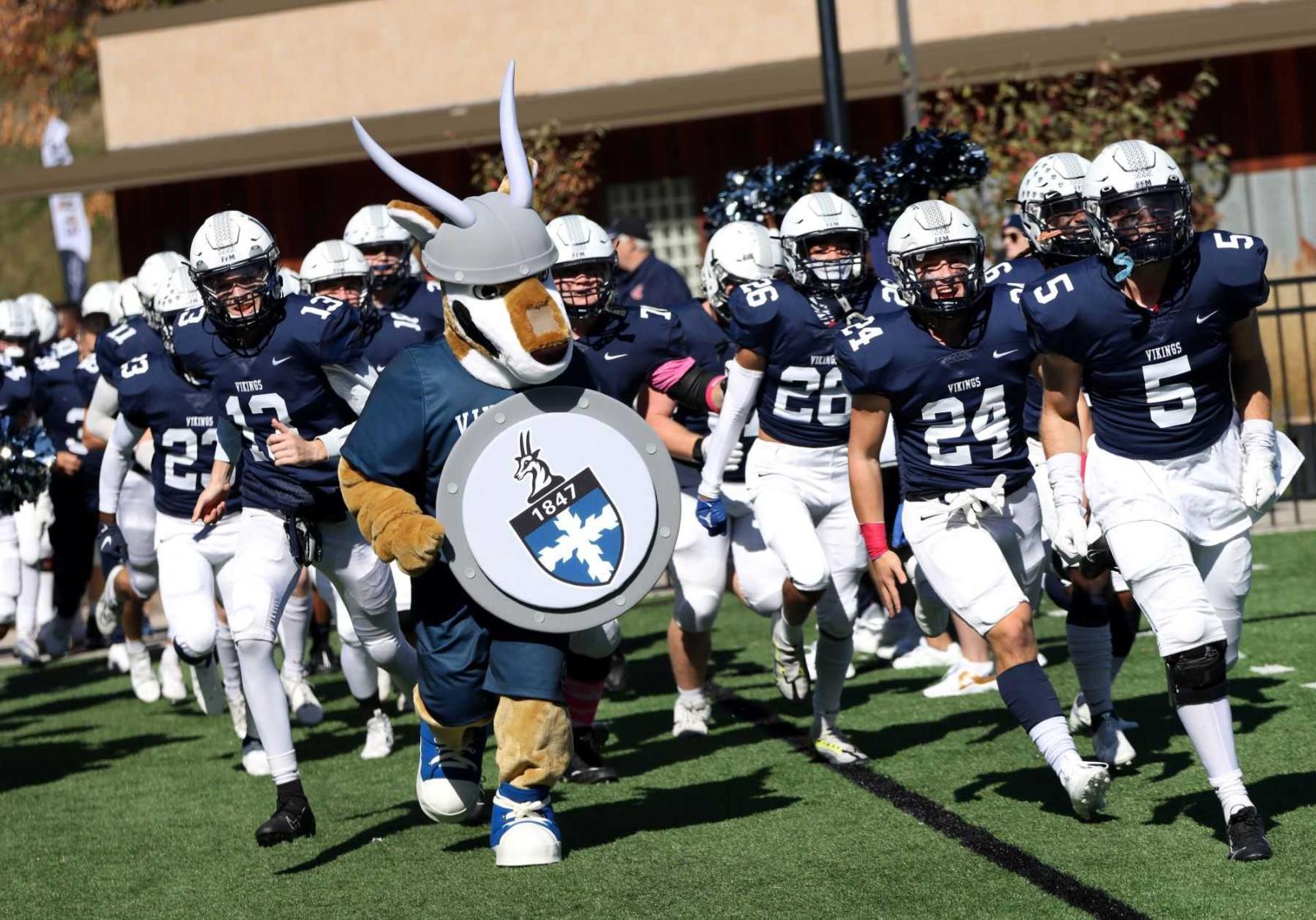 The antelope mascot dressed in Viking gear and carrying a shield with the Lawrence crest leads the football team onto the field before the game.