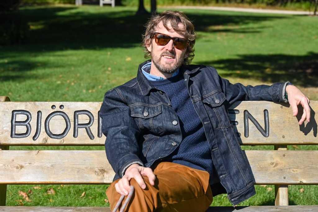 Tom McKenzie poses for a photo on a bench carved with the name Bjorklunden.