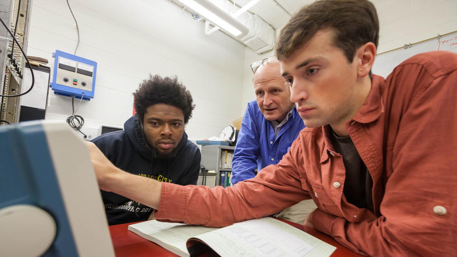 Physics students and faculty reviewing an instrument in a lab