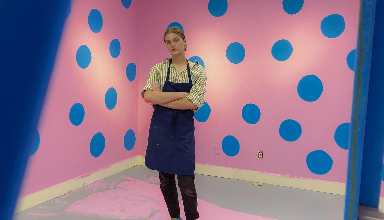 Charlie Wetzel poses for a photo in the middle of a pink and blue art installation.