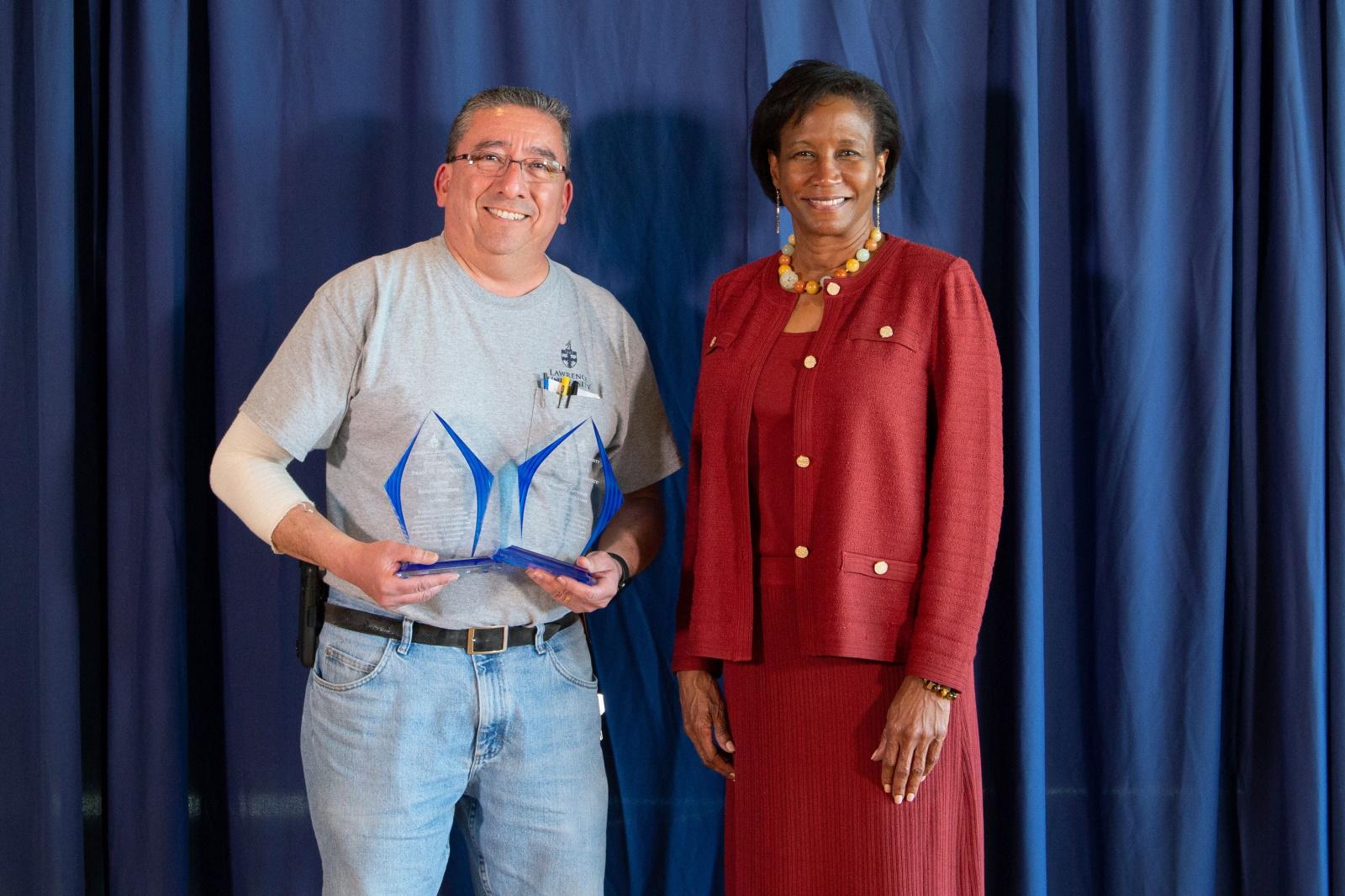 Bob Guzman holds his two awards as he poses for a photo with President Laurie Carter.