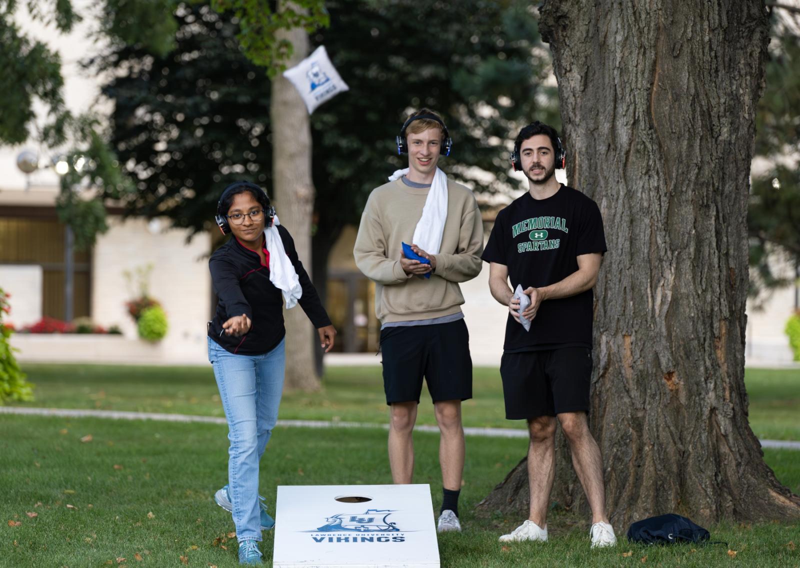 Three students play Cornhole on Main Hall Green.