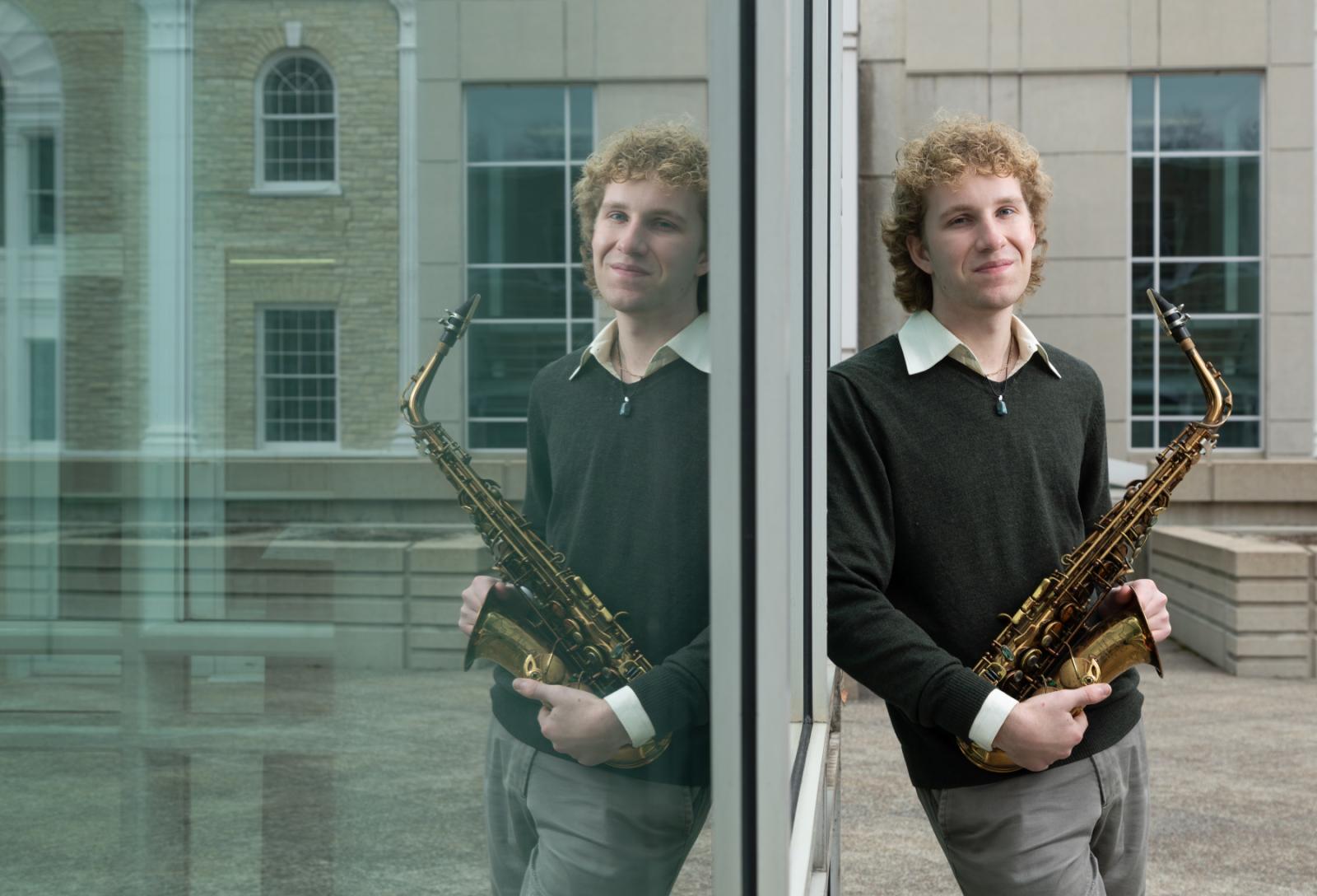 Owen Brady, holding his saxophone, is reflected in the window of Shattuck Hall.