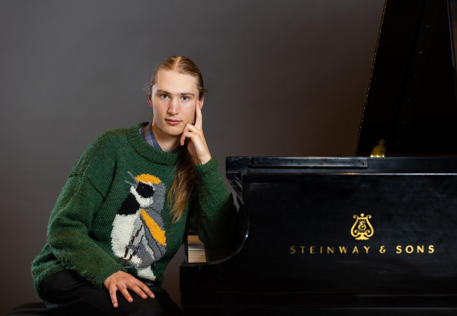 Kai Frueh poses next to a piano wearing a green bird sweater.
