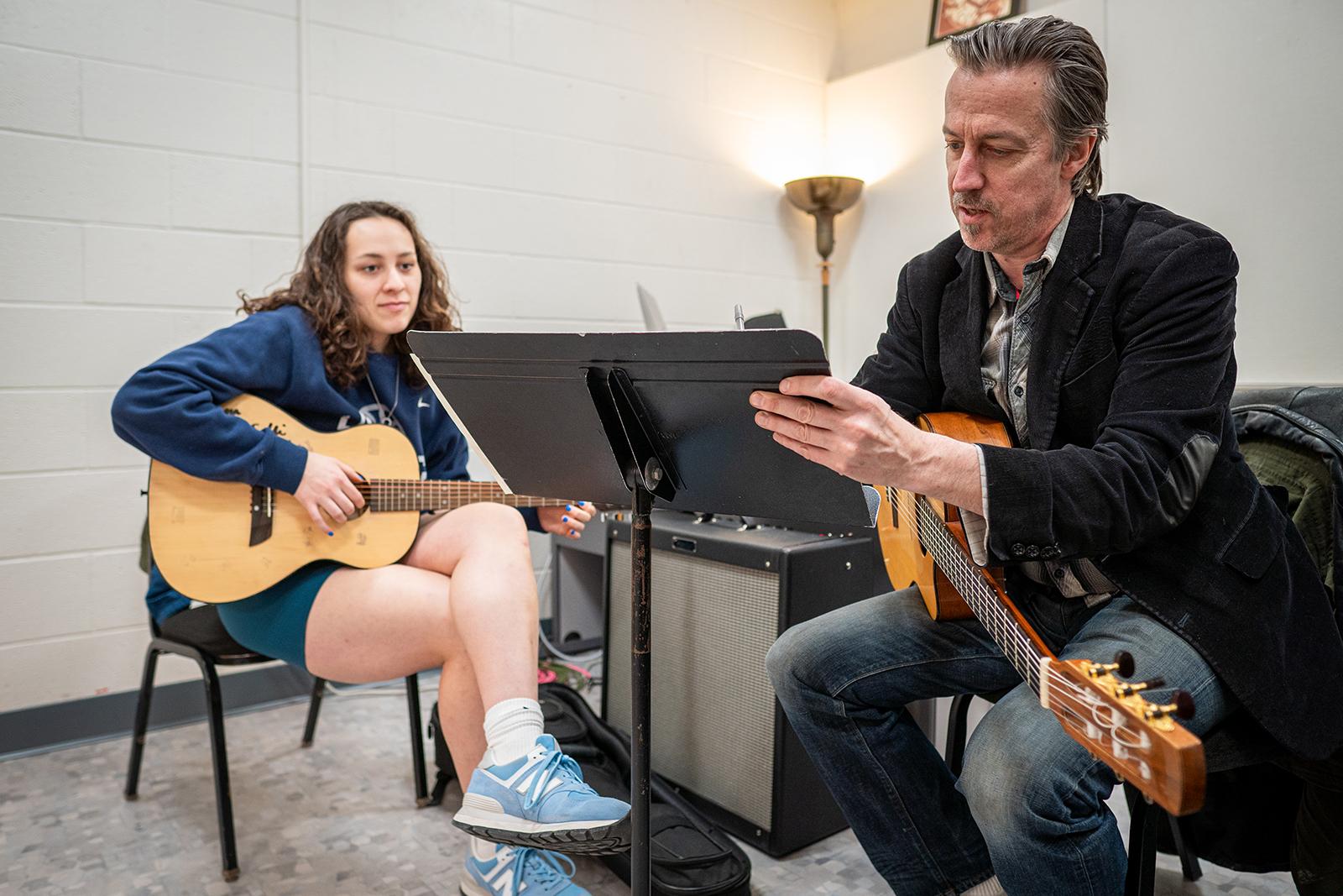 A student receiving a guitar lesson from a teacher.