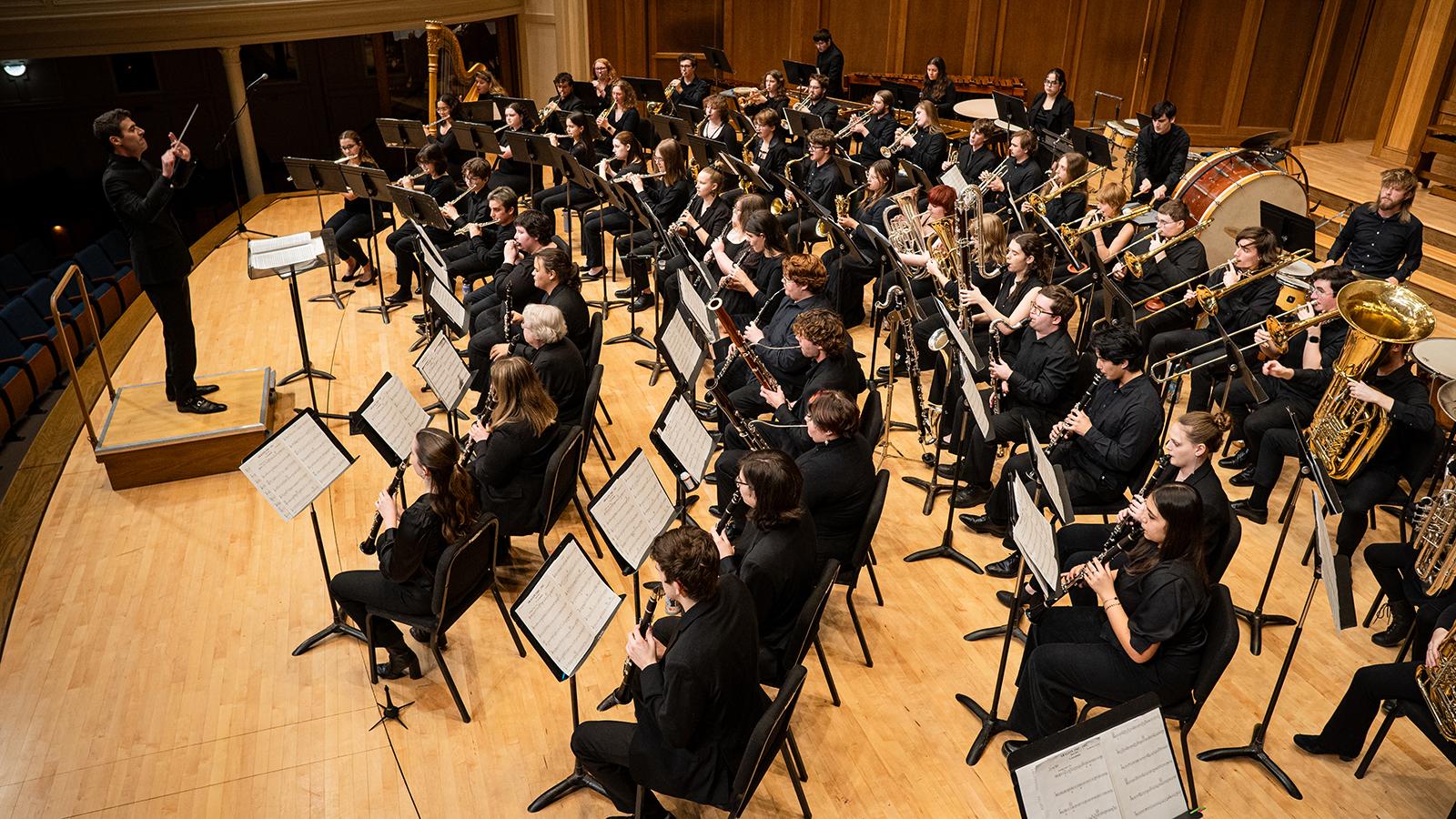 A large wind band led by a conductor.