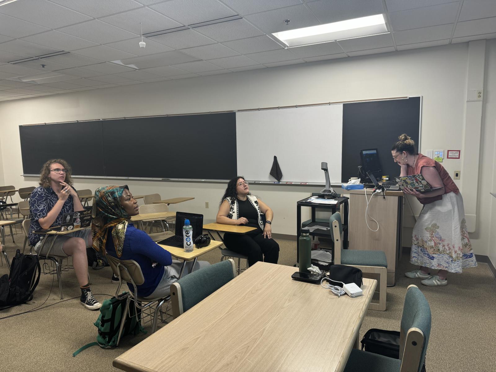 Three people listen to a presenter during ethnic studies summer research.