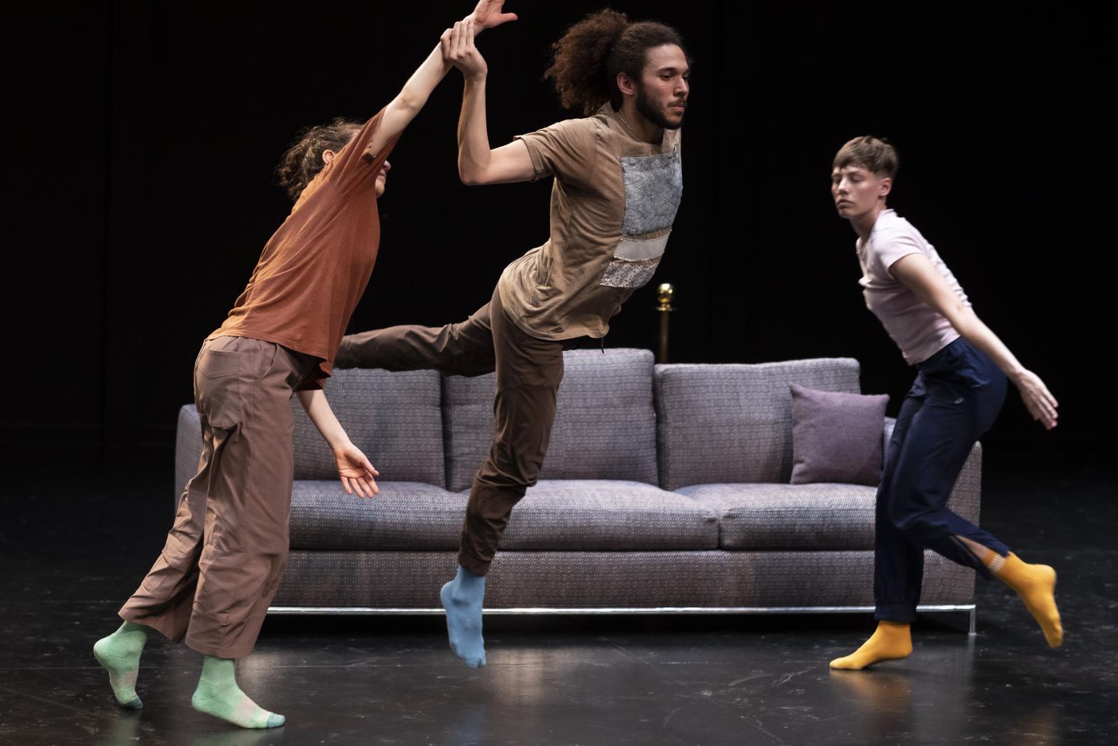 A trio of dancers in motion, with a couch in the background.
