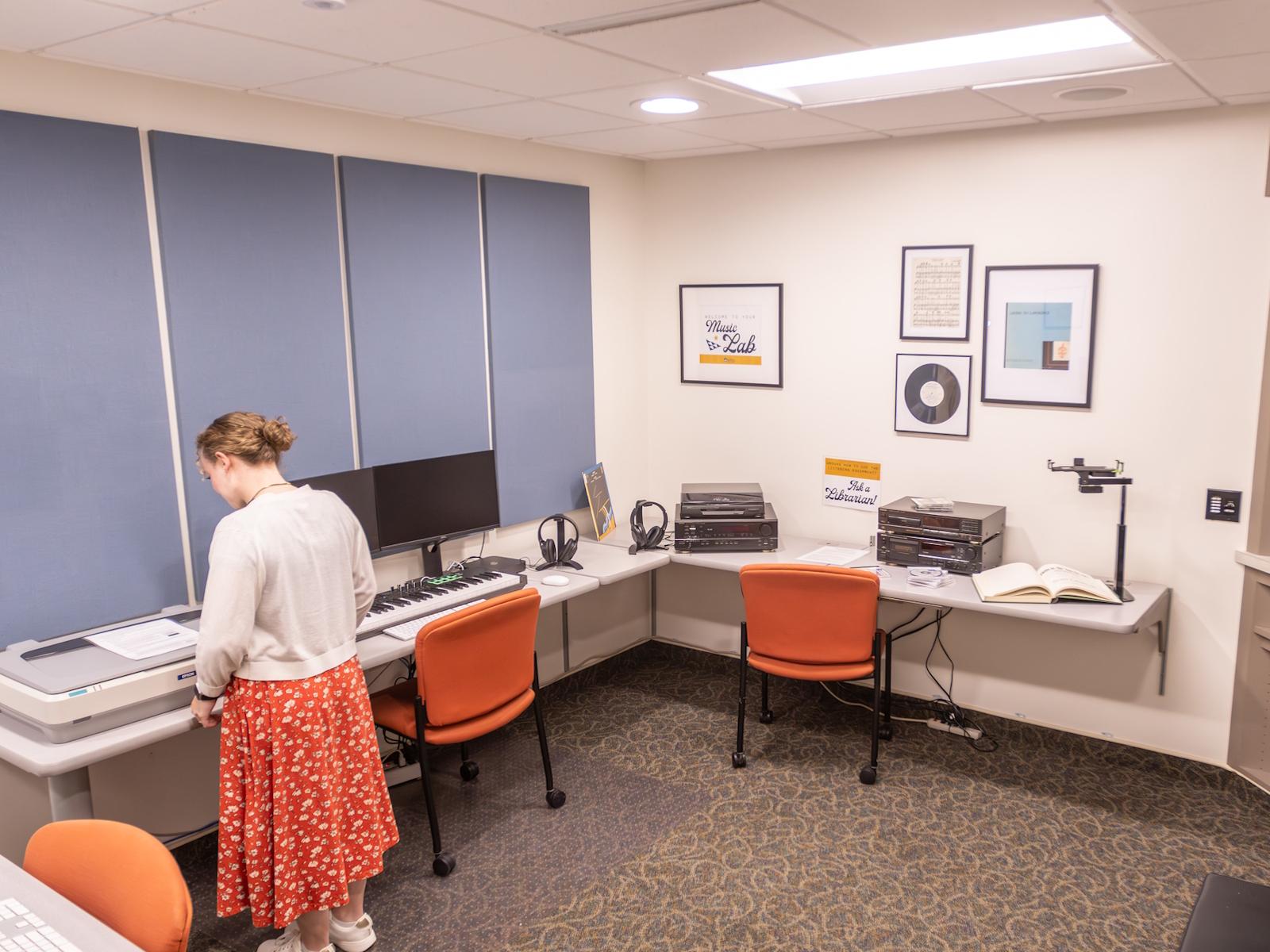 A person with a red skirt standing near the large scanner in the music lab.