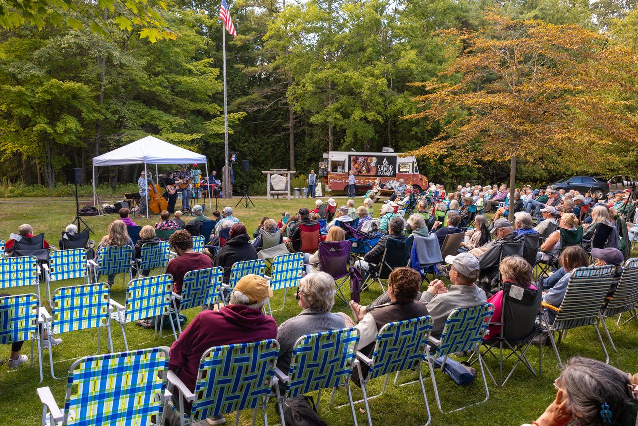 a crowd seated on the lawn in front of the chapel taking in a concert