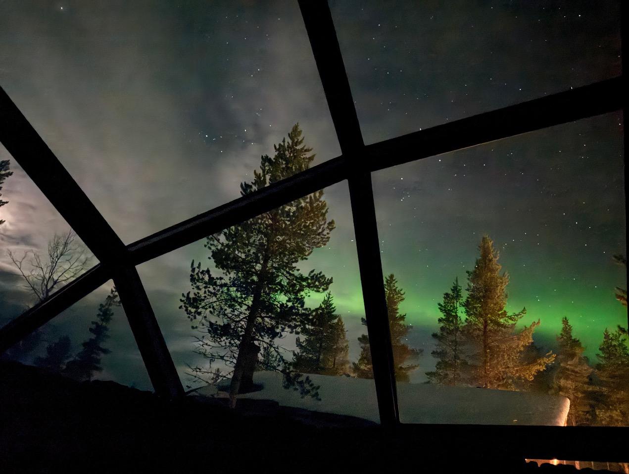 Green northern lights glow in the night sky above a glass igloo in northern Finland.