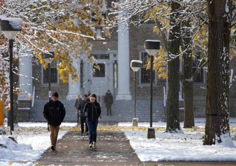 Students walk from Main Hall as snow falls on Main Hall Green.