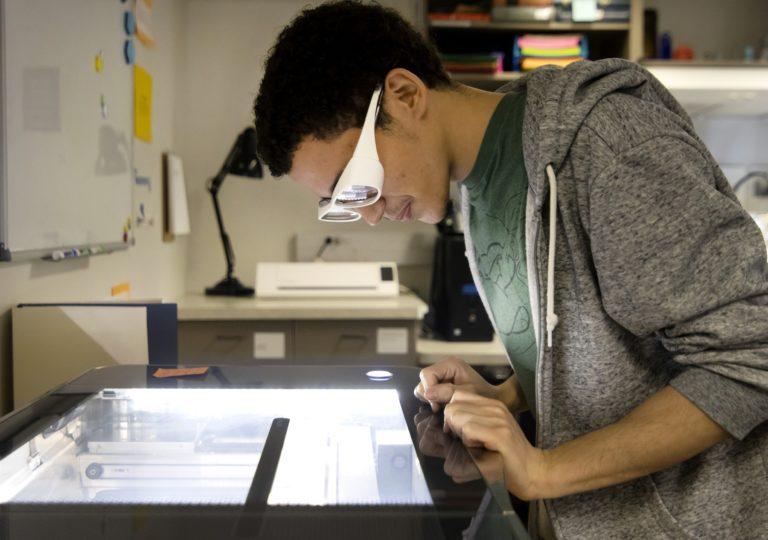 Kelvin Maestre, wearing white goggles, uses a laser cutter in the Makerspace.