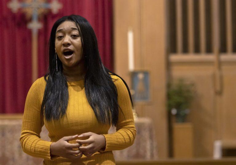 Hannah Jones sings in a church, wearing a yellow sweater.
